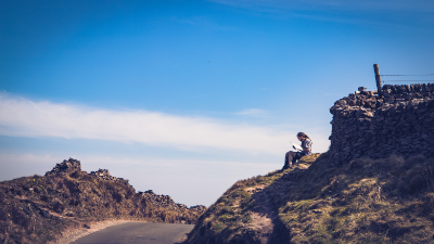 A man reading a book by the side of the road in the Peak District