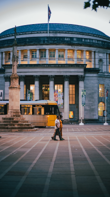 A couple walking through St Peter's Square in Manchester as a tram passes by